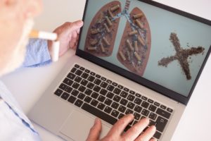 Adult man holds a broken cigarette in his mouth over laptop, to quit smoking. World no tobacco day